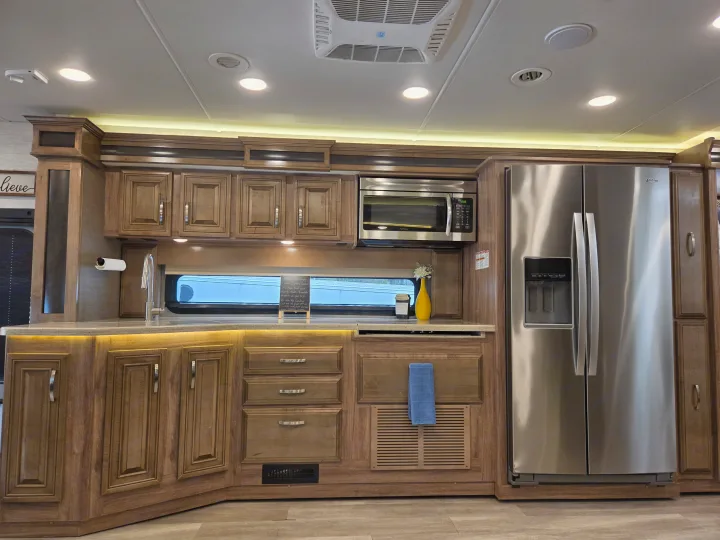 Spacious RV rental kitchen featuring light wood cabinetry, stainless steel appliances, and task lighting over the counters.. Jayco Seneca 2021