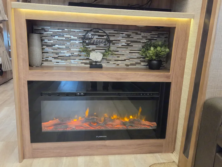 Cozy RV rental interior with an electric fireplace, decorative backsplash, and illuminated shelf with 'Blessed' sign & plants. Homey travel setup.. Jayco Seneca 2021