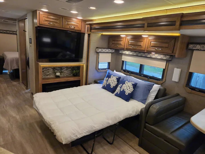 Spacious RV rental interior with a pull-out bed, mounted TV, wooden cabinets, and dining area, offering comfortable living space.. Jayco Seneca 2021