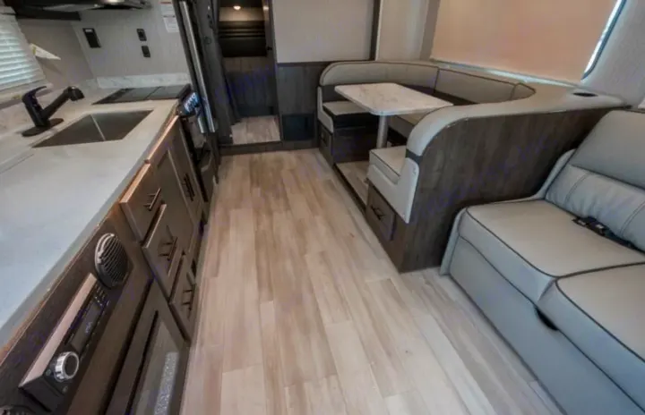 Bright RV rental interior with kitchen, U-shaped dinette, and sofa. Light wood floors and modern grey tones.. Coachmen Leprechaun 2022