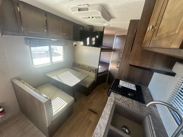 Modern rv rental interior featuring a dinette, functional kitchen with sink & stovetop, mounted TV, and bunk beds.. Keystone RV Coleman 2019