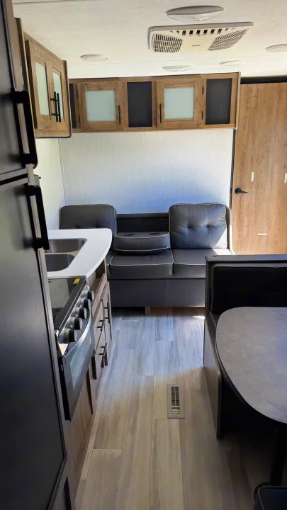 RV rental interior: kitchen with stove, sofa lounge, and dining booth. Features wood-look flooring and overhead cabinets.. Heartland RVs Pioneer 2021