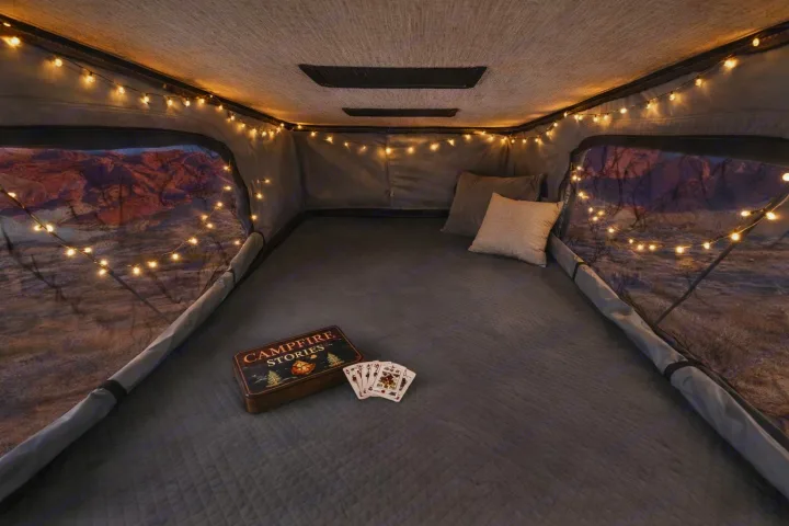 Cozy RV rental interior for glamping. String lights illuminate a comfy bed, scenic views, and Campfire Stories with playing cards.. Winnebago Solis 2026