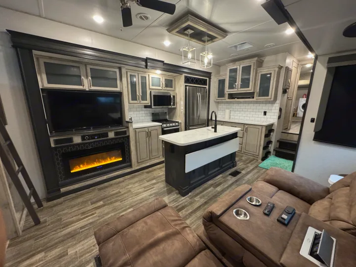 Modern RV rental interior with a fully equipped kitchen, living area featuring a large TV, electric fireplace, and cozy recliners.. Keystone RV Avalanche 2021