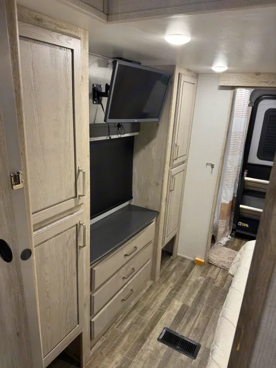 Modern RV rental interior featuring a compact bedroom, wall-mounted TV, and built-in wood-look storage cabinets and drawers.. Keystone RV Avalanche 2021
