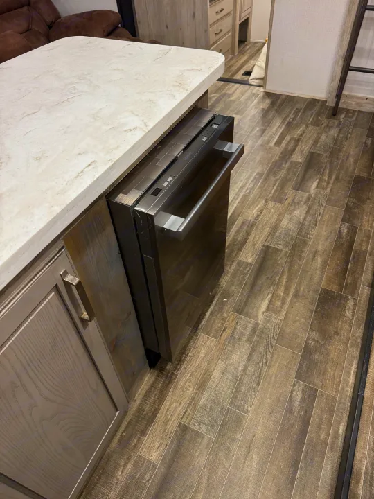Modern RV rental kitchen featuring a dark built-in dishwasher, marbled counter, and wood flooring.. Keystone RV Avalanche 2021