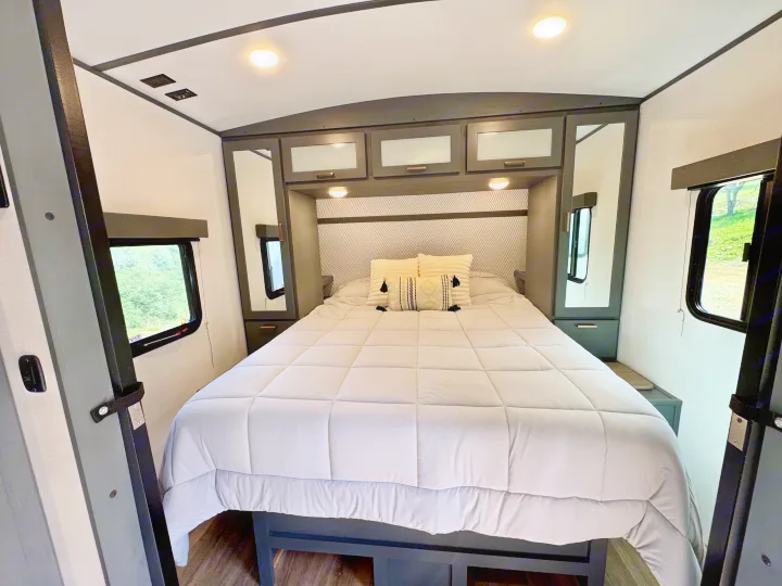 Cozy RV rental bedroom with a comfortable bed, stylish headboard, overhead storage, and dual windows. Ideal for travel trailer stays.. Keystone RV Bullet Ultra Lite 2023