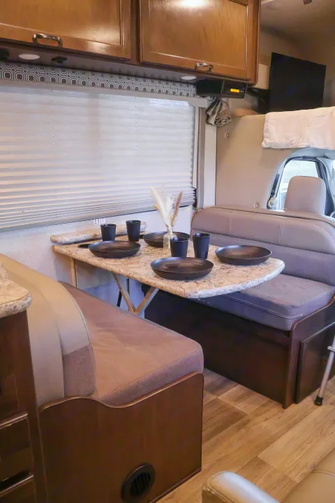 RV rental interior: A fully set dinette with black dishes, plush bench seating, and wood cabinets, ready for meals.. Thor Four Winds 2017
