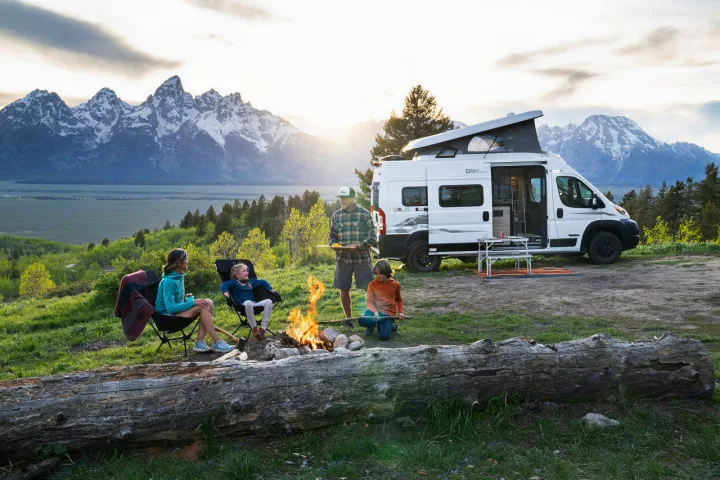 Family enjoys an RV rental camping trip, gathered by a campfire with majestic mountains & sunset views.. Winnebago Solis 2025