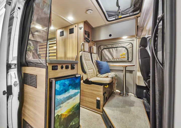 Inside a modern rv rental camper van, featuring a cozy seating area, compact kitchen, and unique fridge design.. Winnebago Solis 2025