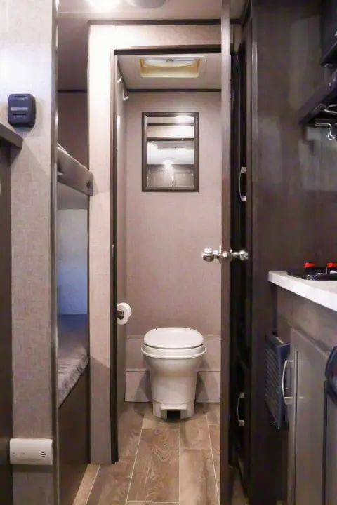 View of an rv rental interior: hallway to compact bathroom with toilet & mirror, bunk beds (left), and kitchen counter (right).. Jayco Baja 2021