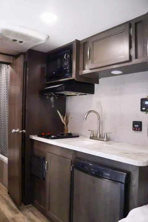 Compact RV rental kitchen featuring a microwave, stovetop, sink, and refrigerator in a modern design for travel.. Jayco Baja 2021