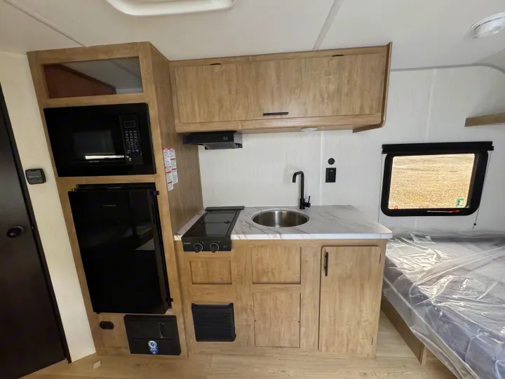 RV rental: Modern kitchenette in a travel trailer, featuring microwave, fridge, sink, stove, wood-grain cabinets, and a bed.. Forest River WOLF PUP 17LP 2026