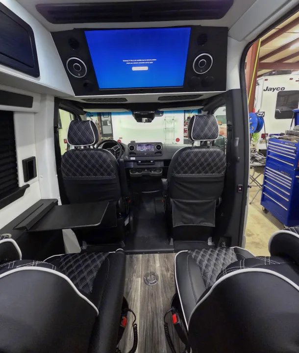 Inside a luxurious rv rental: plush black leather seats, an overhead TV displaying a network error, and dashboard controls upfront.. Mercedes 3500XD 2023