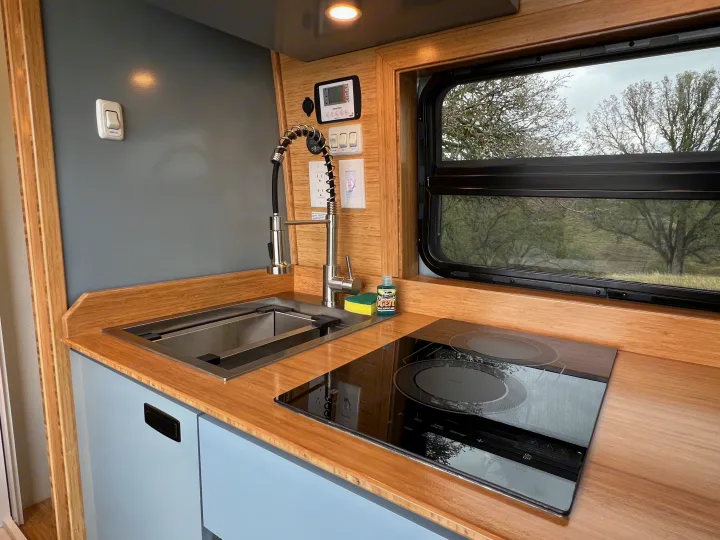 Well-equipped rv rental kitchen with a stainless steel sink, pull-down faucet, induction cooktop, and a scenic window.. Mercedes-Benz Sprinter 2024