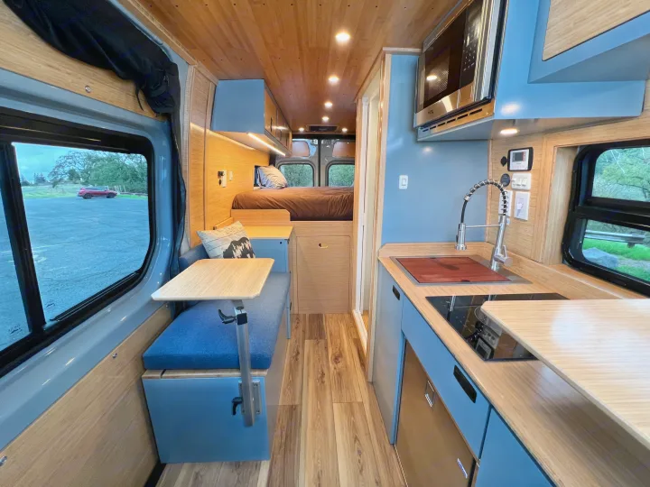 This RV rental shows a modern camper van interior featuring a kitchen, bed, and dining area, ideal for mobile living.. Mercedes-Benz Sprinter 2024