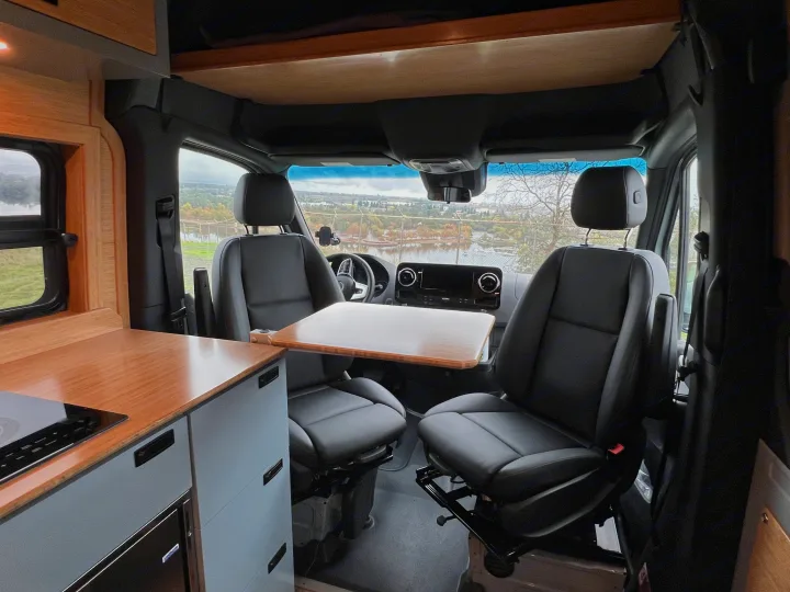 Inside this RV rental, front swivel seats face a portable table and kitchenette, offering scenic views for travelers.. Mercedes-Benz Sprinter 2024
