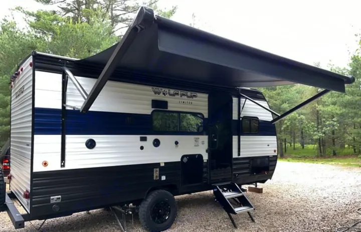 RV rental: a white & blue travel trailer with black awning extended, steps down, parked on gravel with pine trees.. Forest River Cherokee Wolf Pup 2024