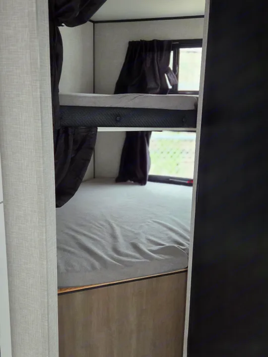 RV rental bunk beds: a compact interior sleeping area with grey bedding, windows, and dark privacy curtains.. Open Range Conventional 26BHS Travel Trailer 2025
