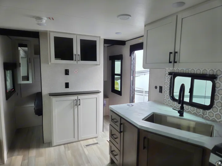 Interior view of an RV rental kitchen, featuring a sink, light countertops, white cabinets, and modern backsplash.. Open Range Conventional 26BHS Travel Trailer 2025