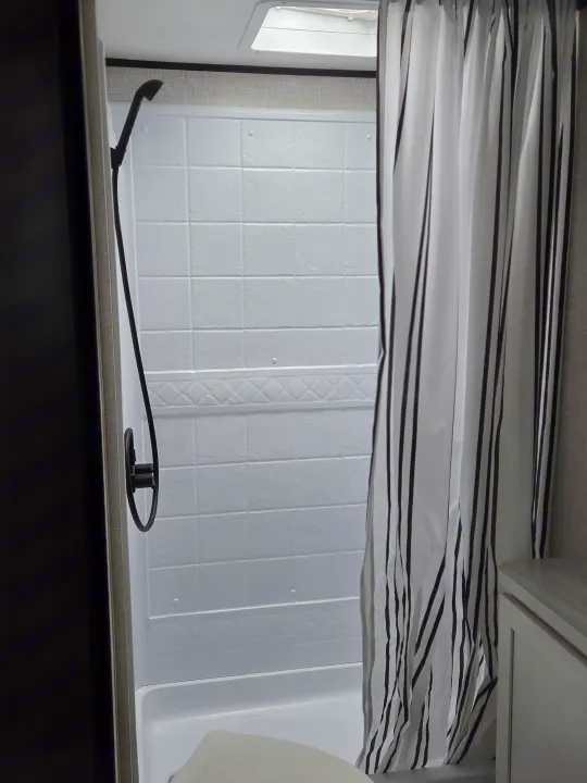This RV rental's compact wet bath features white tiled walls, a black shower, and a striped curtain. Efficient for camping.. Open Range Conventional 26BHS Travel Trailer 2025