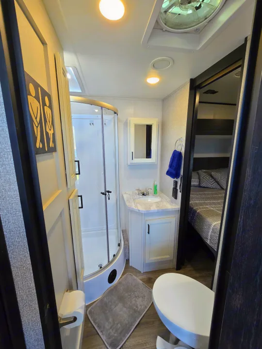 Bright RV rental bathroom features a glass shower, sink vanity, toilet, and bedroom view, maximizing space for travelers.. Highland Ridge RV Mesa Ridge 2021