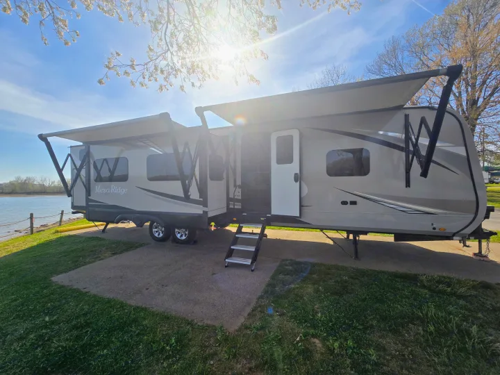 Experience nature with this RV rental: a Mesa Ridge travel trailer parked by a sunny waterfront. Awnings extended for comfort.. Highland Ridge RV Mesa Ridge 2021