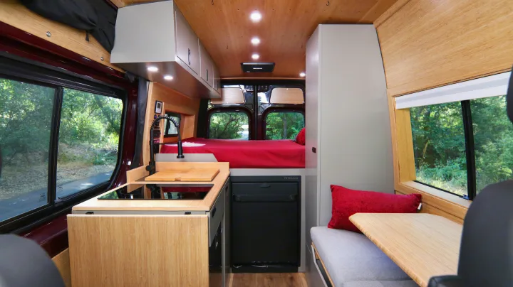 This RV rental interior showcases a modern camper van with a compact kitchen, raised bed, and a cozy dinette.. Mercedes-Benz Sprinter 2025