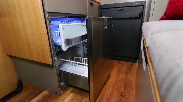 Modern RV rental kitchen featuring an open fridge with freezer drawer, a Tetravan unit, and a cozy bed area.. Mercedes-Benz Sprinter 2025