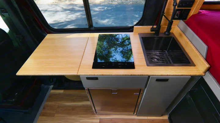 RV rental kitchen area: modern bamboo counter, induction cooktop, black sink, and fridge. Great for travel.. Mercedes-Benz Sprinter 2025