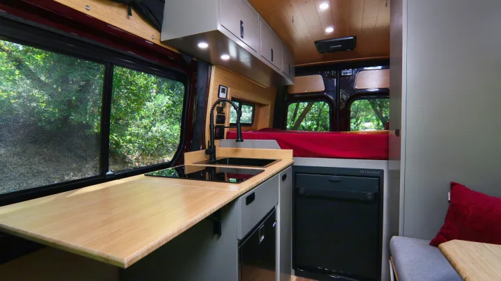 Experience this rv rental: a compact interior featuring a modern kitchen with sink & stove, comfy bed, and lush window views.. Mercedes-Benz Sprinter 2025