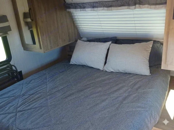 Inside this RV rental, find a comfortable bedroom with a gray bed, light pillows, and window blinds. Wood cabinets add storage.. Forest River Palomino Puma XLE Lite 2021
