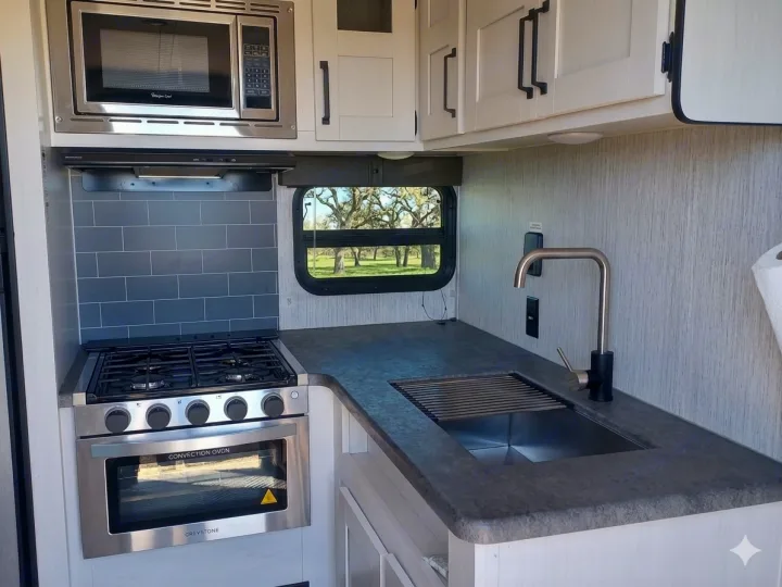 Modern RV rental kitchen with stainless microwave, Greystone convection oven, stove, sink, and subway tile backsplash.. Forest River Palomino Puma XLE Lite 2021