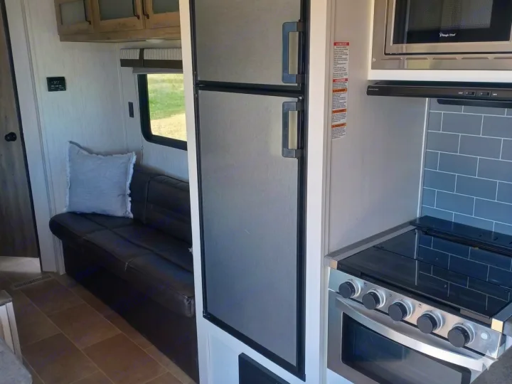 RV rental with a modern kitchen: stainless steel fridge, microwave, and oven/stove, plus a cozy dark sofa with a pillow.. Forest River Palomino Puma XLE Lite 2021