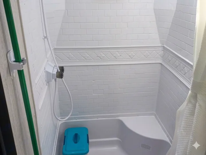 Bright white RV rental shower features faux subway tile, decorative trim, built-in seat, handheld shower, and a blue storage bin.. Forest River Palomino Puma XLE Lite 2021