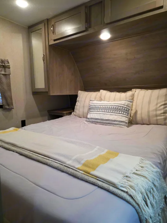 Serene RV rental bedroom: light gray bedding, striped pillows, and wooden overhead cabinets for a cozy stay.. Palomino puma 2020
