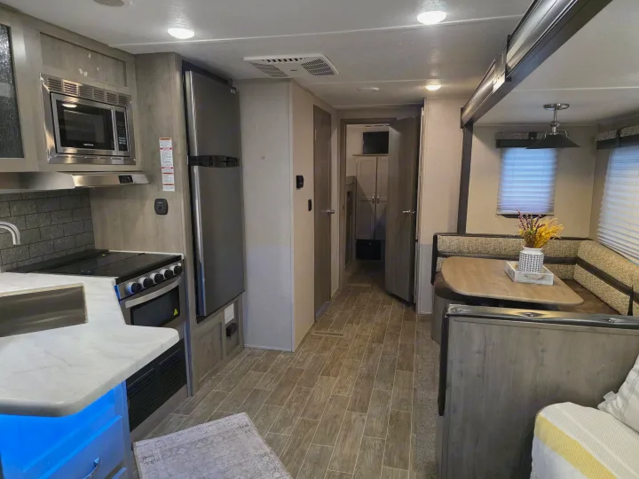 This RV rental's modern interior features a full kitchen with a microwave and stove, a dining booth, and a hallway leading to other rooms.. Palomino puma 2020
