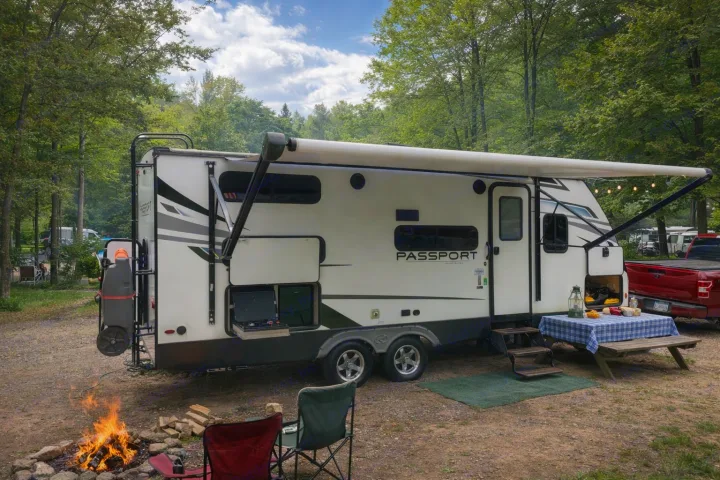 Cozy rv rental campsite: A Passport travel trailer with an extended awning, picnic table, and a warm campfire.. Keystone RV Passport 2022