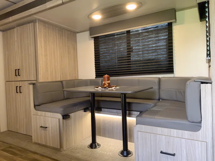 RV rental dinette features cozy booth seating, light wood cabinetry, and a black table with a decorative candle.. Keystone RV Passport 2022