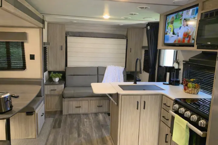 Explore this modern rv rental interior, featuring a compact kitchen, dining booth, and a sofa with a pull-down bed.. Keystone RV Passport 2022