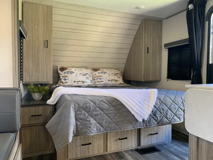 Cozy rv rental bedroom: bed with fish pillows, wood-paneled walls, overhead cabinets, and under-bed storage.. Keystone RV Passport 2022