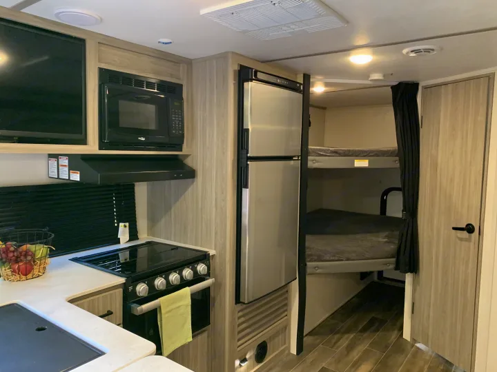 RV rental interior: A compact kitchen featuring a black stove, microwave, stainless steel fridge, and cozy bunk beds.. Keystone RV Passport 2022