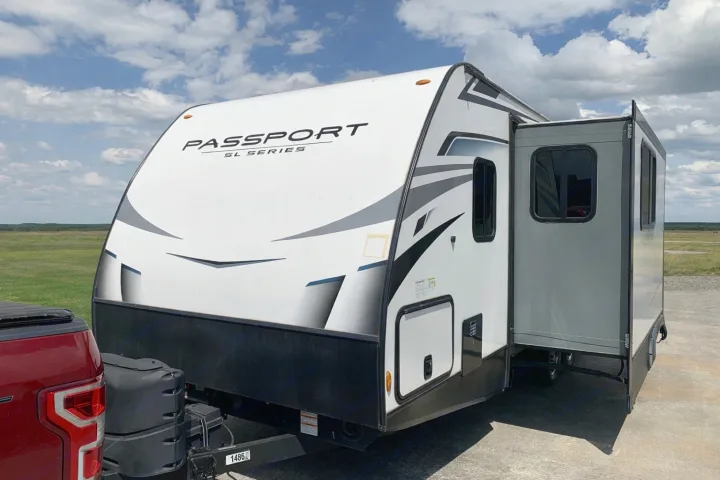 White Passport SL Series travel trailer with slide-out extended, hitched to a truck. Perfect for your next rv rental trip.. Keystone RV Passport 2022