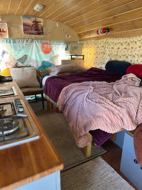 Cozy RV rental interior features a comfortable bed, compact kitchenette, and decorative tapestries, plus essential safety equipment.. GMC Vandura 1986