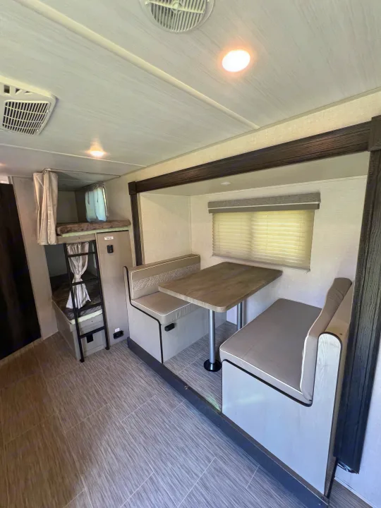 Bright rv rental interior featuring a dinette, bunk beds with ladders and privacy curtains.. Forest River Ibex 2021