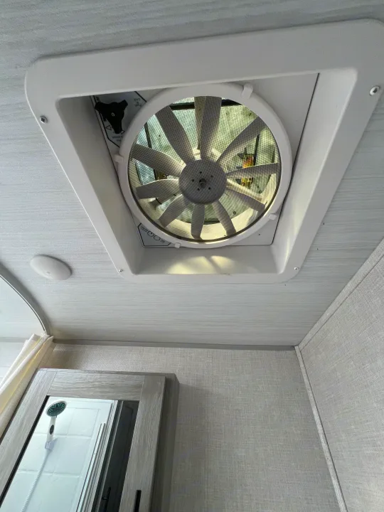 RV rental bathroom interior: A ceiling fan/vent with controls is visible overhead, and a shower head reflects in the mirror.. Forest River Ibex 2021