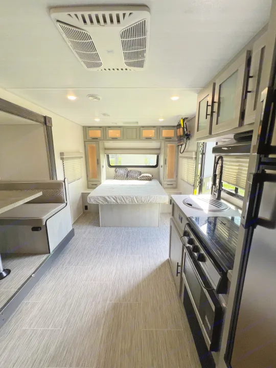 Light-filled rv rental interior featuring a modern bedroom, full kitchen with stove, and comfortable dinette seating.. Forest River Ibex 2021