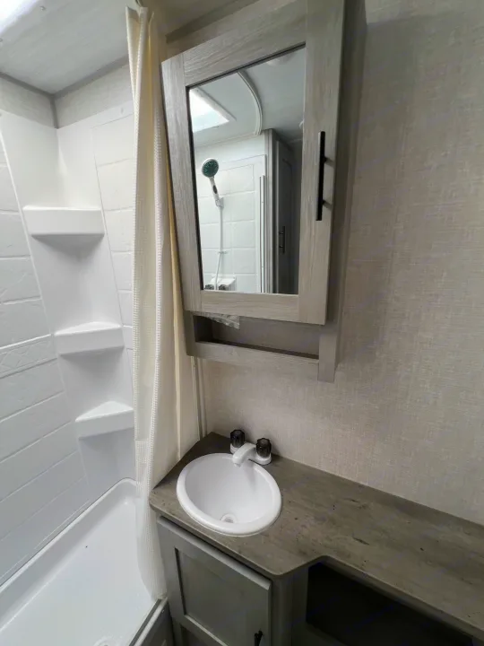Inside a clean rv rental bathroom, featuring a white shower with curtain, vanity with sink, and mirrored cabinet.. Forest River Ibex 2021