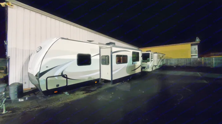 RV rental at night: A large travel trailer with its slide-out extended is parked next to a building, with another RV behind it.. Cruiser RV MPG Ultra Lite 2017