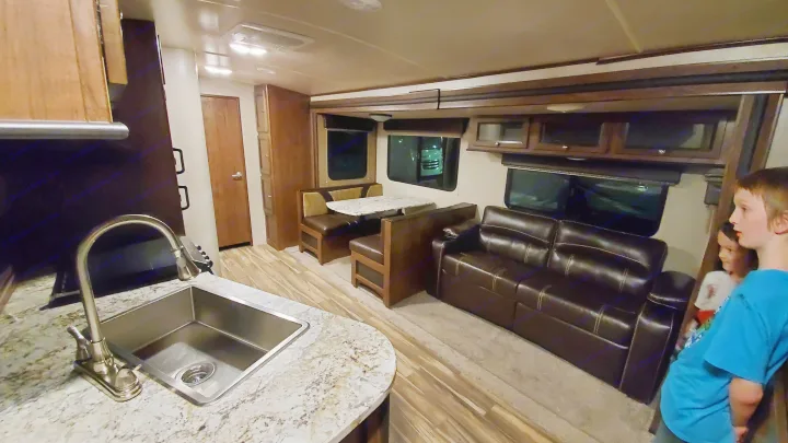 Spacious RV rental interior with a full kitchen, dinette, and sofa. Children are visible in this cozy living space.. Cruiser RV MPG Ultra Lite 2017